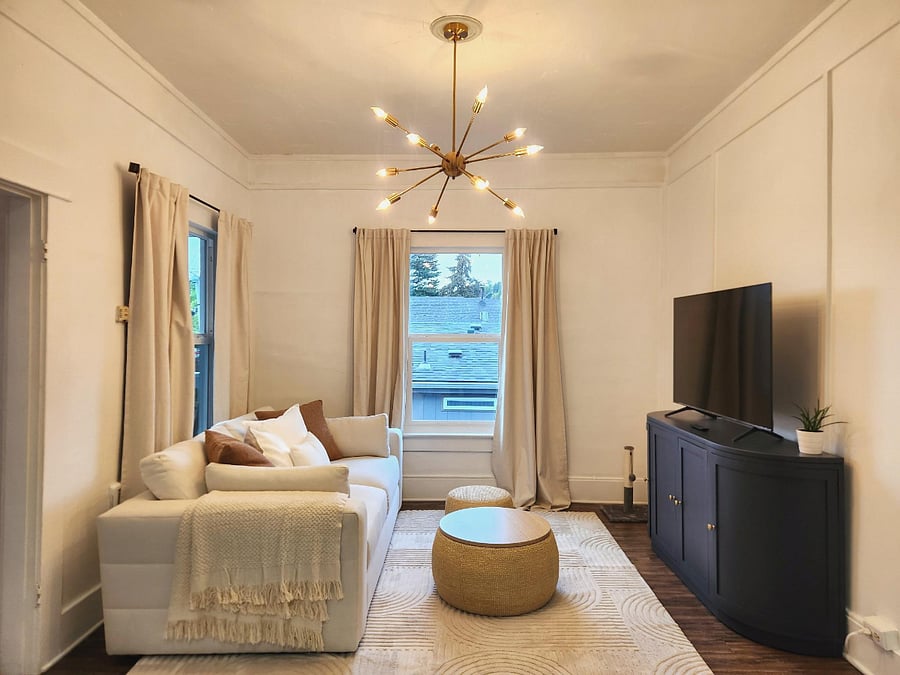 Living room with deep seated couch, smart TV, blackout curtains and large storage cabinet.