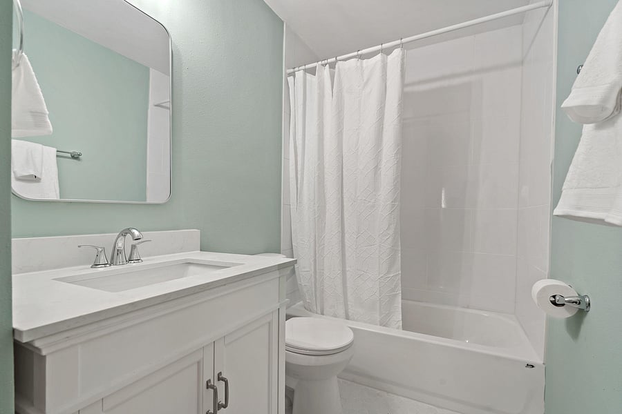 Clean full bathroom with a single-sink vanity, large mirror, and tub/shower combo with tile surround for easy upkeep.