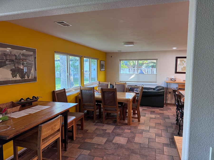 Spacious dining area with large table seating, adjacent lounge space, and multiple windows overlooking the yard.