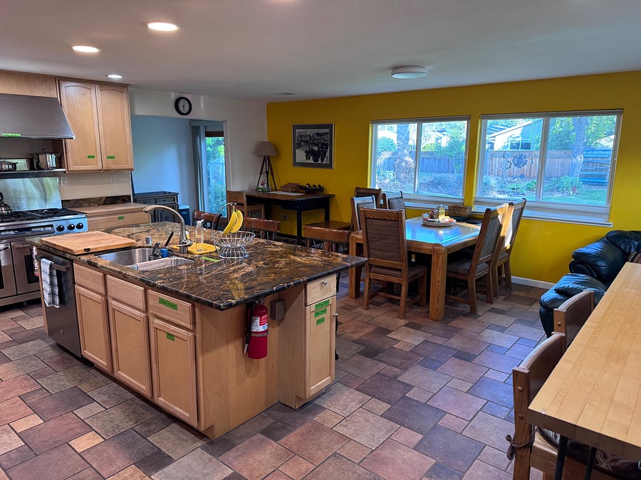 Open kitchen with a spacious island, gas range, and ample cabinetry, flowing into a dining area with large backyard-facing wi