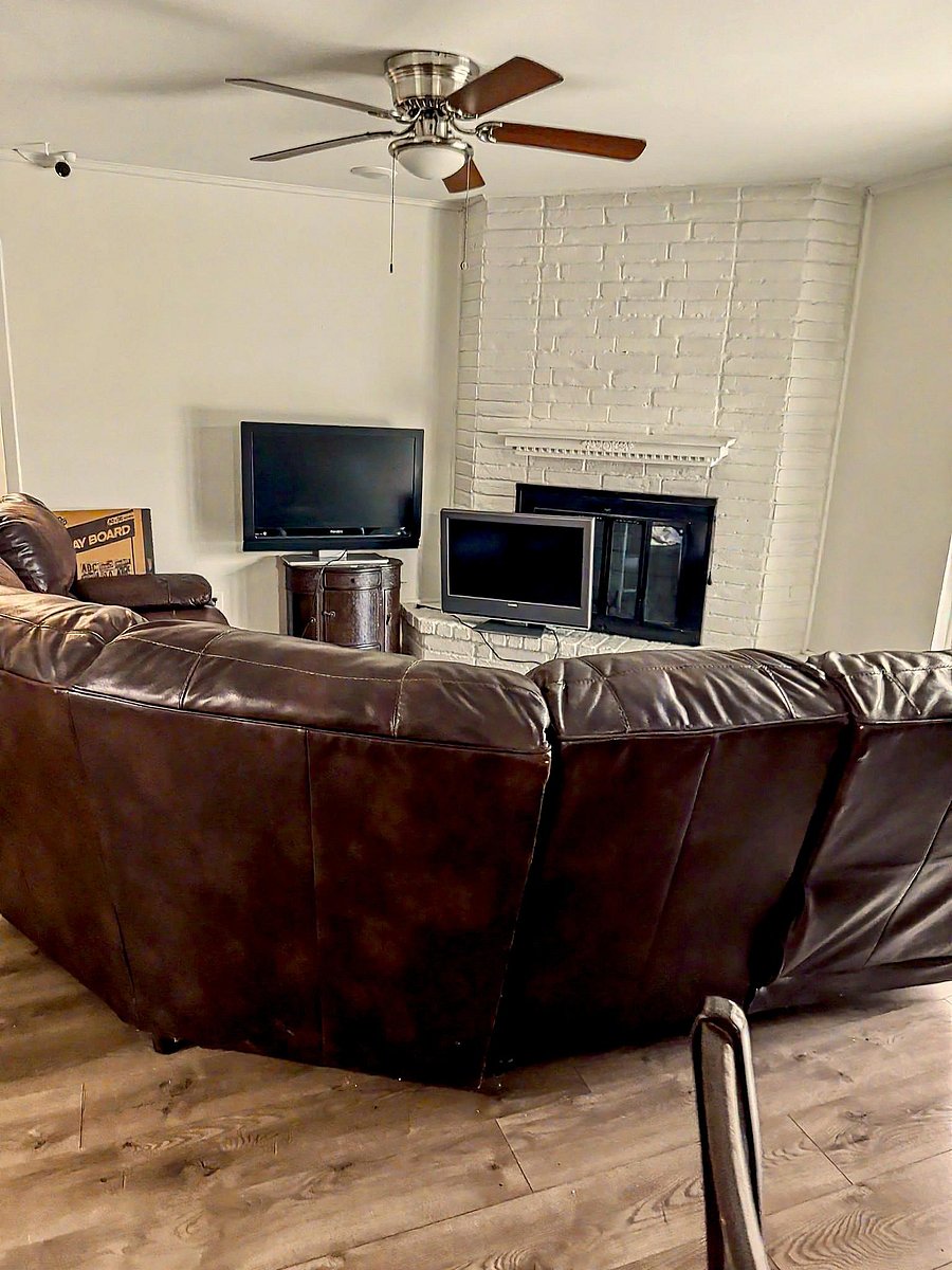 Shared living room with a large sectional, ceiling fan, and a painted brick fireplace as a focal point for relaxing.