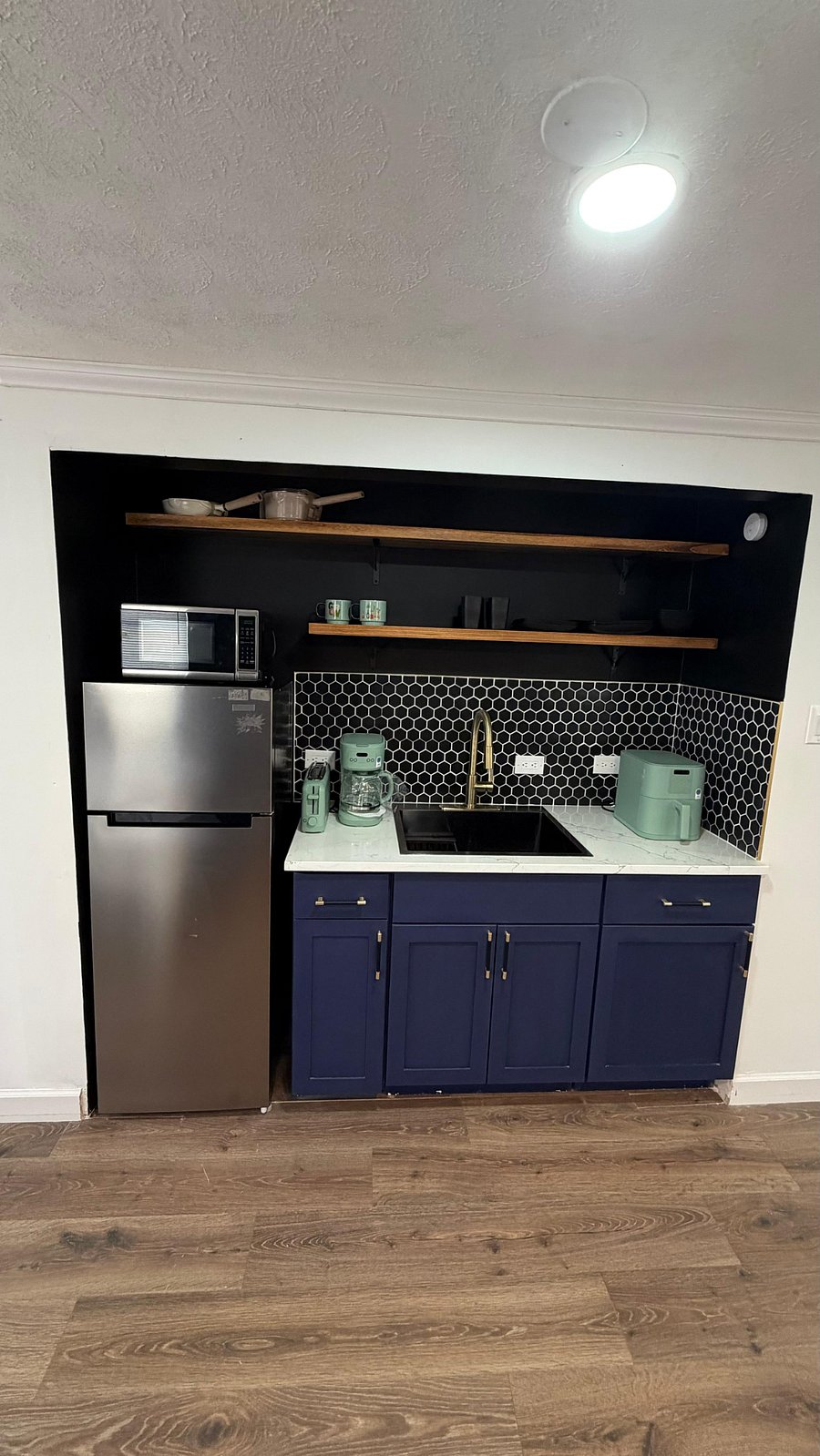 Half kitchen with cooktop burners, air fryer, microwave, sink, full fridge, toaster, plates/bowls, cups/mugs, cookware, and utensils. 