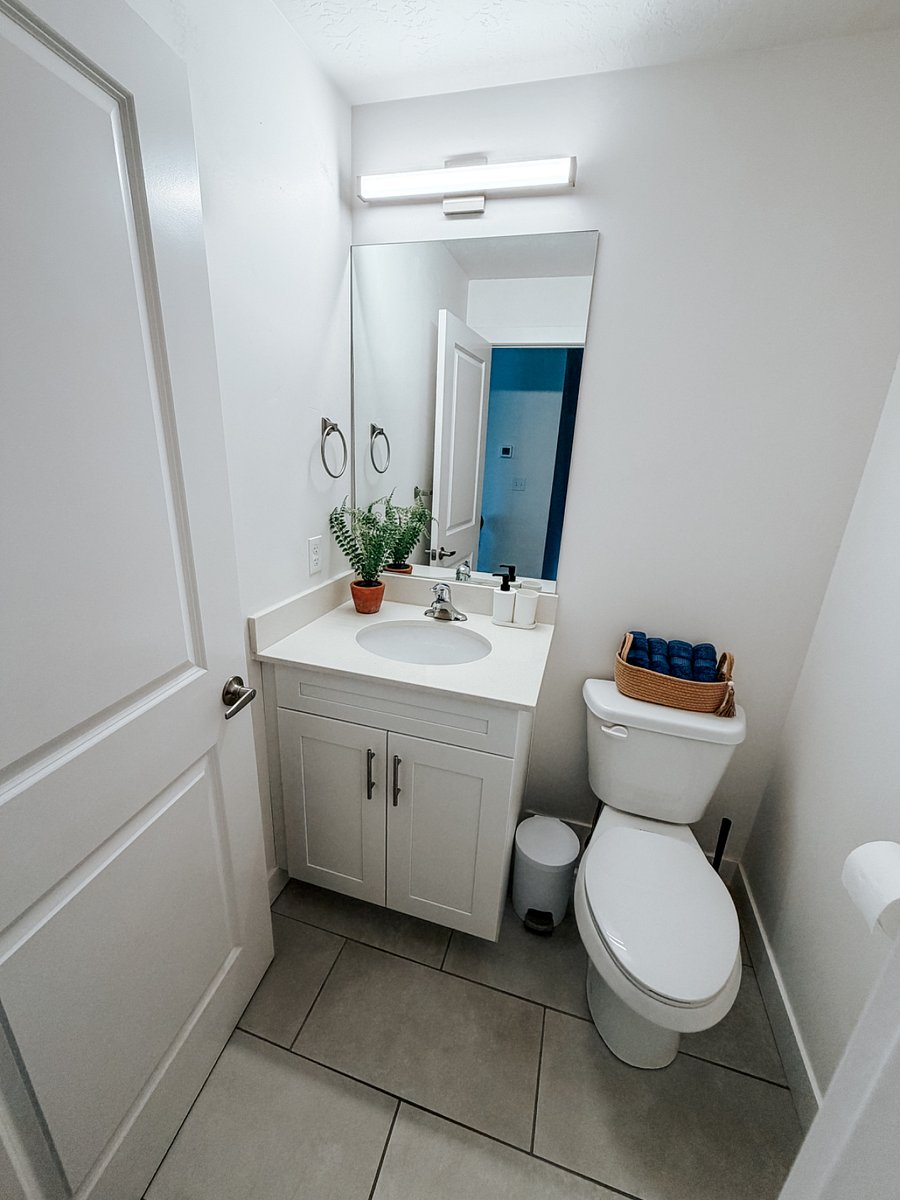 Main Floor Half Bath / Powder Room

Clean and bright half bathroom featuring a white vanity with sink, large mirror with light bar, and convenient storage cabinet. Fresh towels and a plant add a welcoming touch.