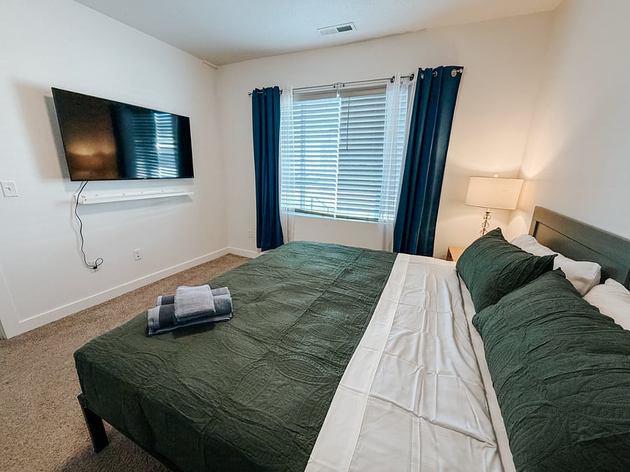 Primary Master Bedroom with Full Bathroom

Spacious first-floor master bedroom featuring a comfortable king bed with green bedding, large window with blackout curtains for better sleep, wall-mounted TV, and direct access to a private full bathroom.