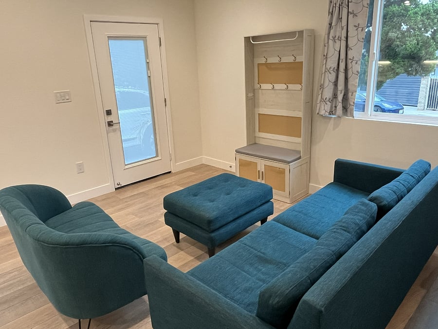 Audreys entry area features a full lite mini blind glass door, and the living room area has a couch, loveseat and ottoman.
