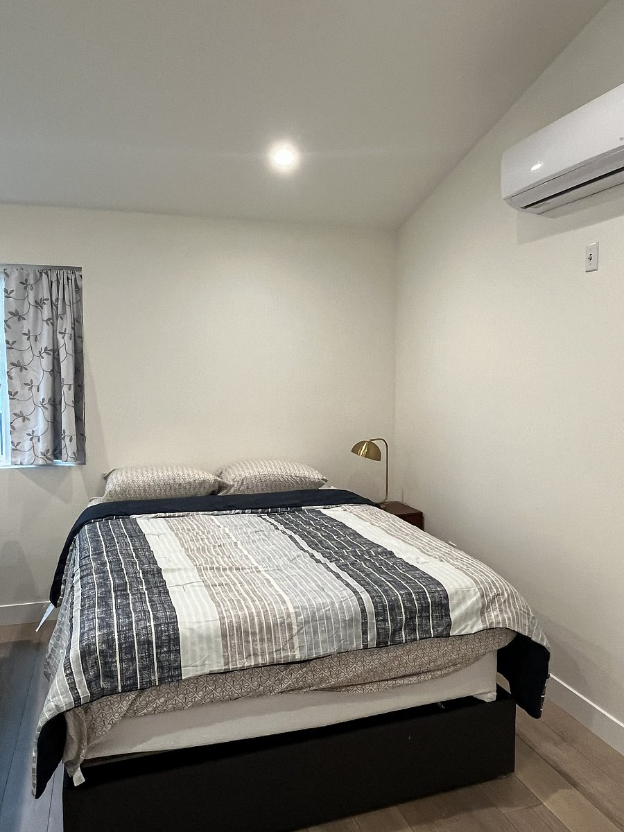 The sleeping area features a queen-sized platform bed with storage drawers underneath. The unit's AC/heat is located on the wall to the right, and a closet is located directly behind the photographer.
