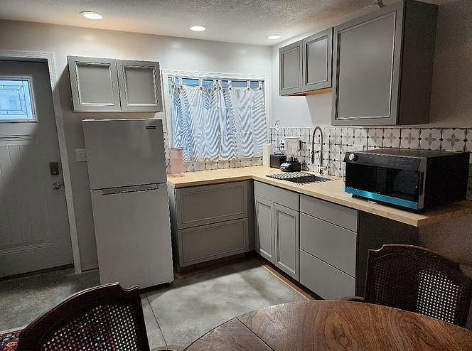 Kitchenette with apartment size refrigerator, electric water pot, blender, toaster, coffee maker, microwave/toaster oven/air fryer, dishes and glasses. Extra cleaning supplies under the sink.

