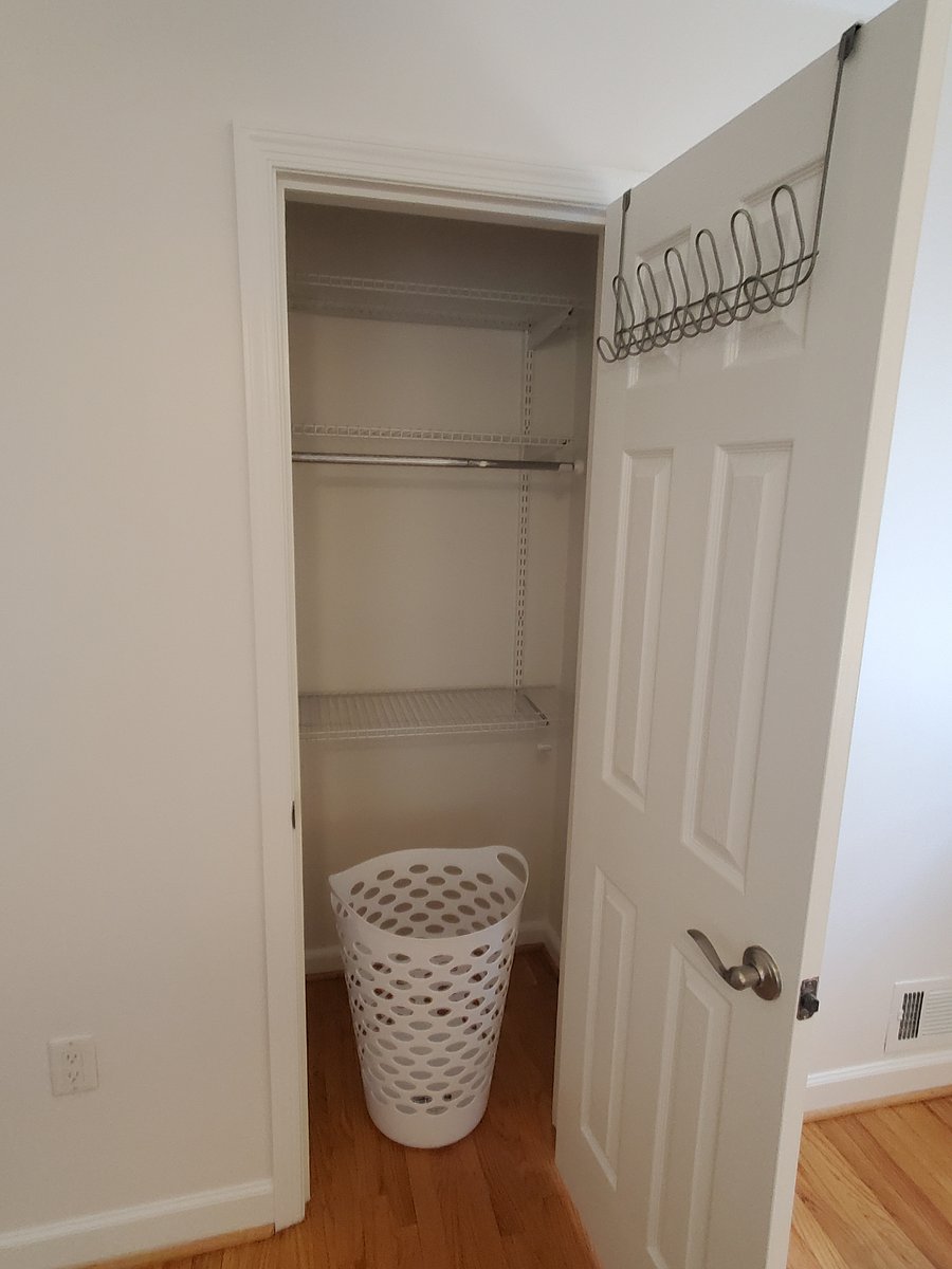 Sizable closet with laundry basket and garment hooks on door.
