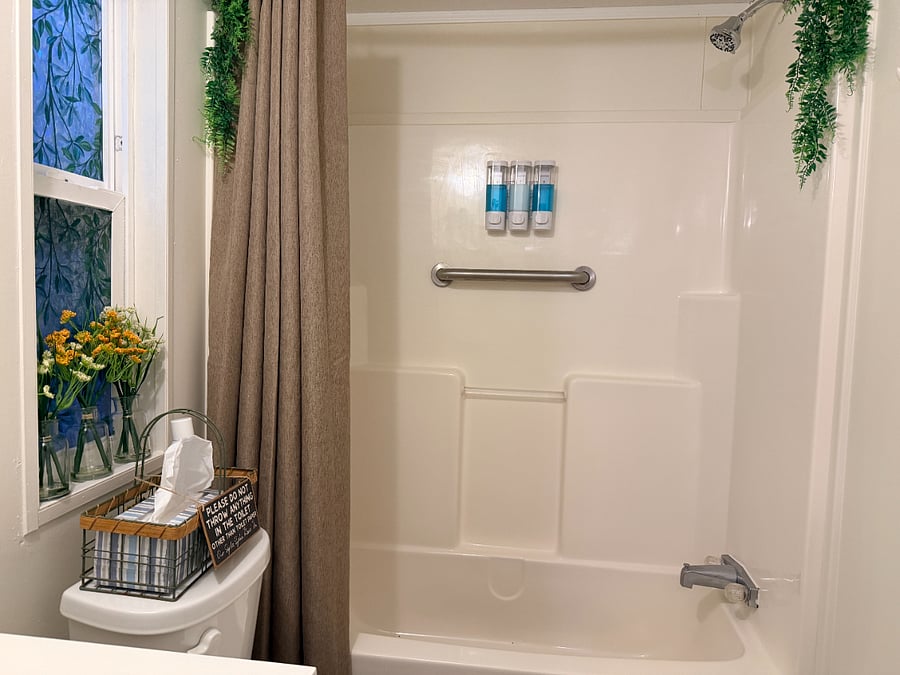 The second bathroom has a bathtub and a shower, with handrails. Shampoo, conditioner, and body wash are on the shower wall.