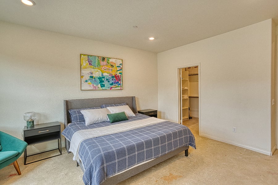 This serene primary bedroom offers a king-sized bed and a spacious walk-in closet. The clean, minimalist design and soft lighting create a perfect environment for rest and relaxation after a busy day in Santa Clarita.