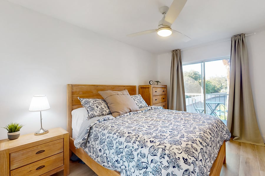 Master bedroom features a plush queen bed and sliding glass doors that lead to private balcony