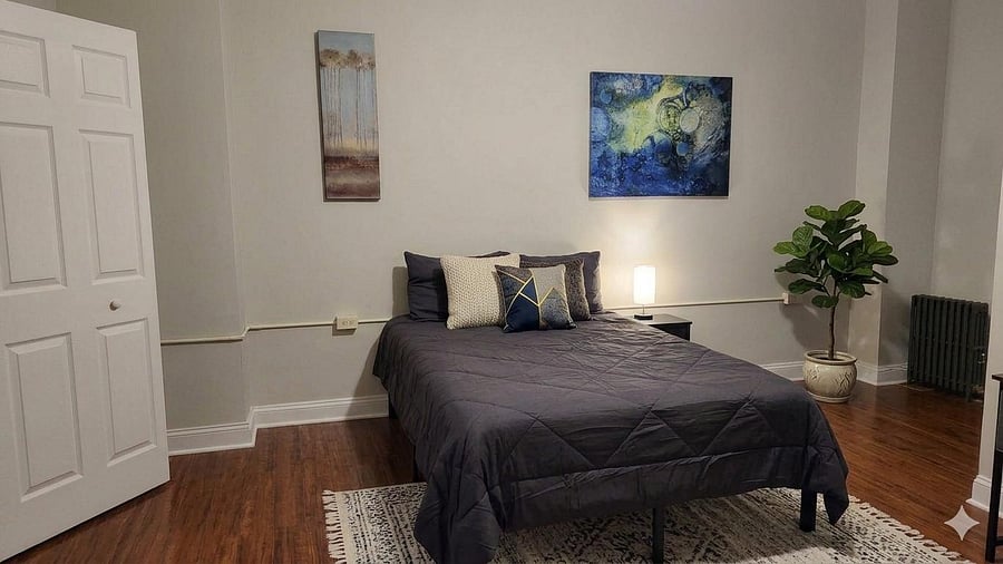 Private bedroom with hardwood floors, a full-size bed, side table lighting, and wall art, plus closet access for storage.