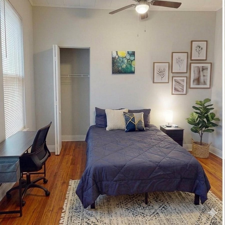 Furnished bedroom with a full-size bed, hardwood floors, a desk workspace, and an open closet for easy storage.