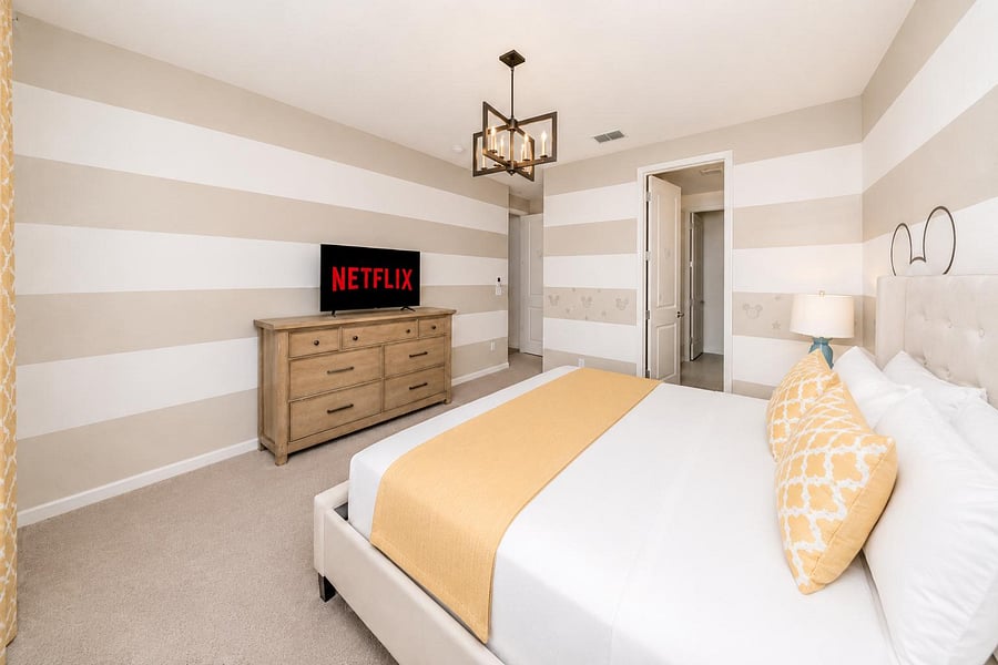 Spacious furnished bedroom with a comfortable bed, dresser with TV, and an en-suite bath for added convenience.