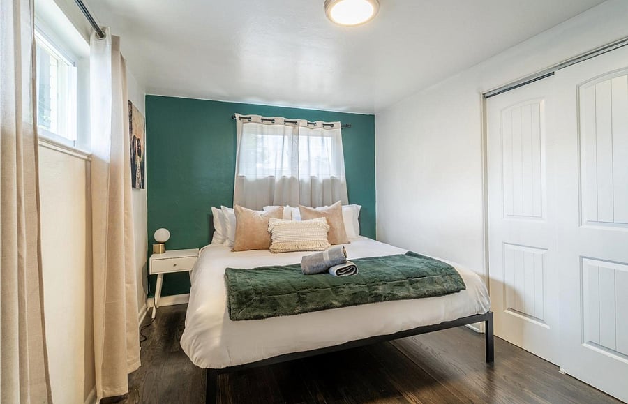 Staged bedroom with a full bed, accent wall, and windows with curtain panels, plus a sliding-door closet for storage.