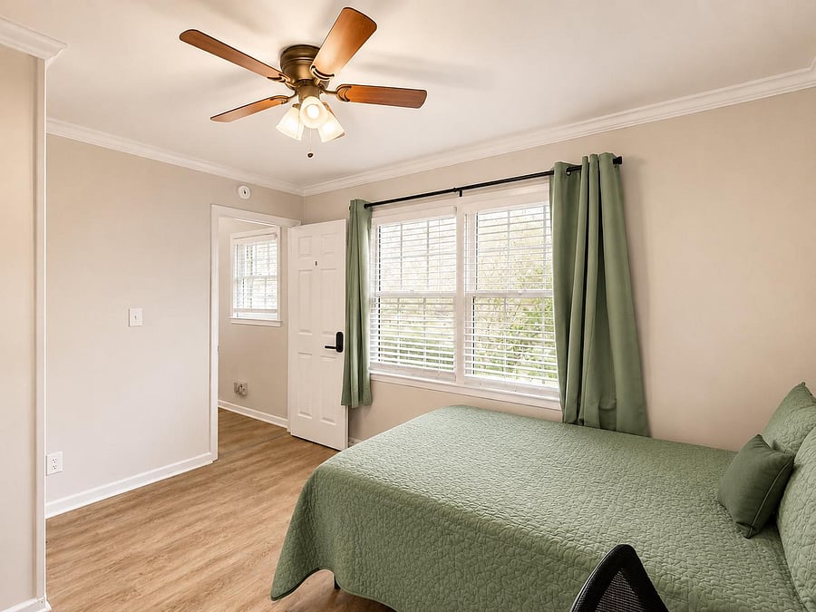 Furnished bedroom with a large window, ceiling fan, and wood-style flooring for a comfortable everyday setup.