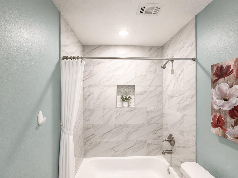 Updated tub/shower combo with marble-look tile surround, built-in niche shelving, and contemporary brushed hardware.