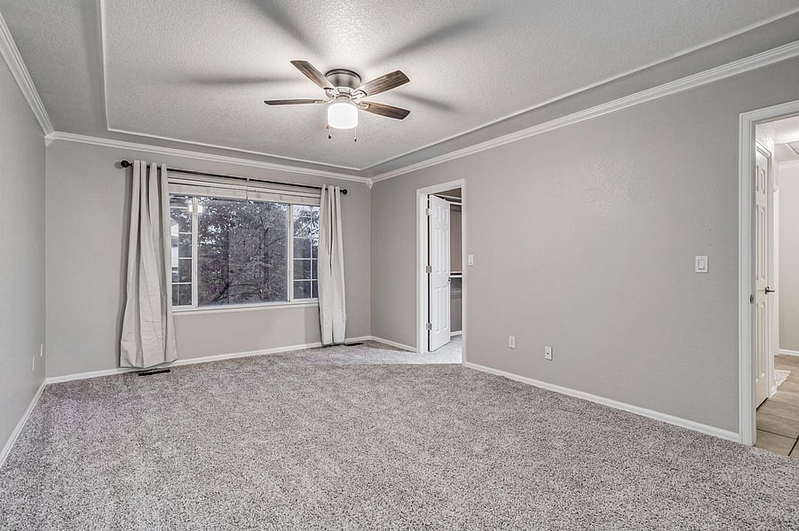 Spacious carpeted bedroom with a large window, ceiling fan, and easy access to a closet and nearby bath.