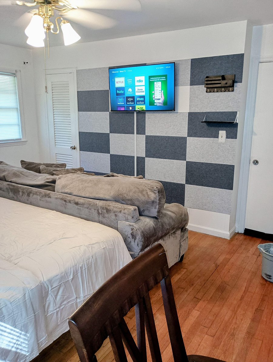 Furnished bedroom with Media wall and hardwood floors, ceiling fan, window blinds, and a wall-mounted TV for easy relaxing.