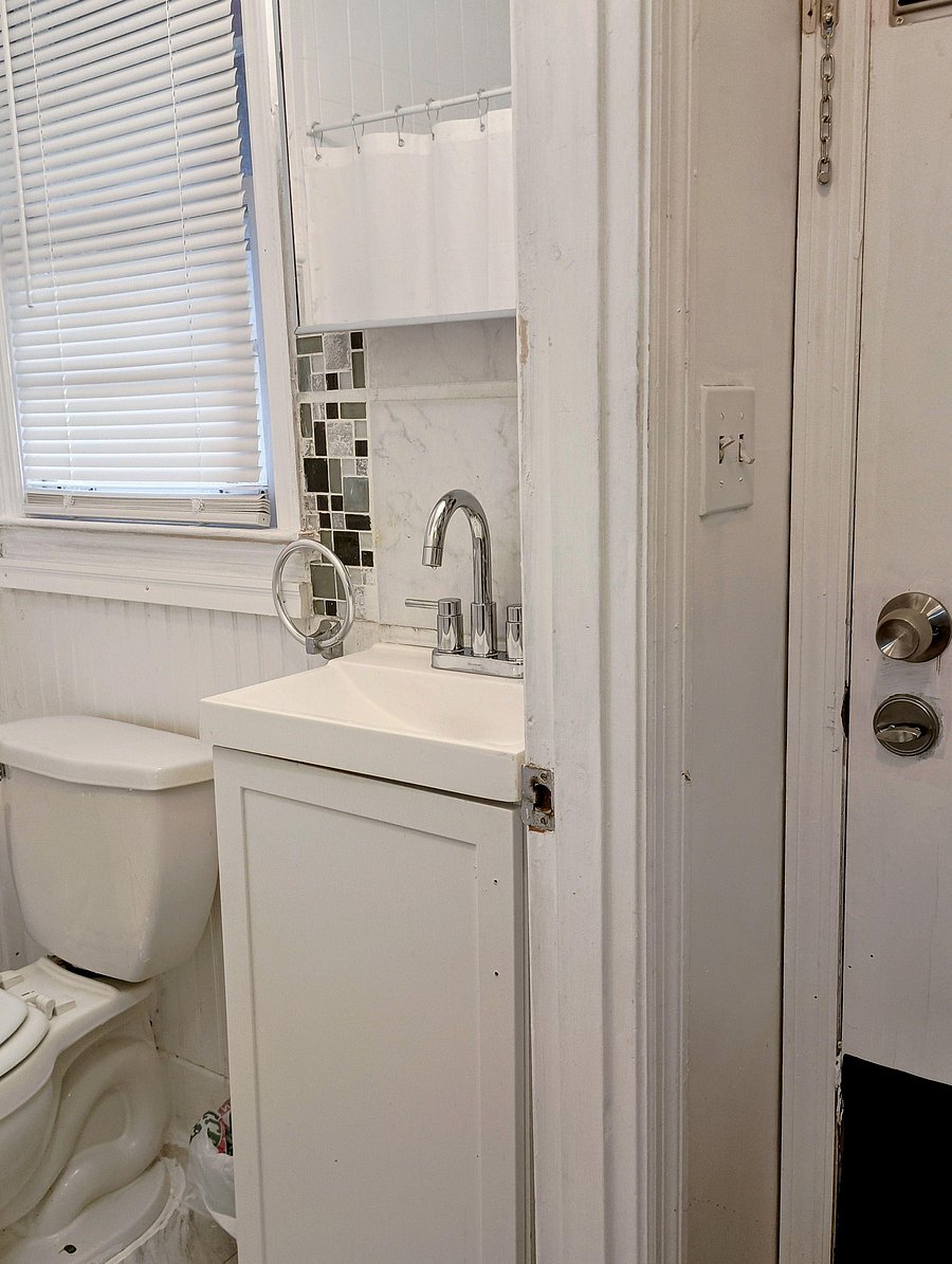 Compact bathroom with a vanity sink, mosaic tile accent, and a window with blinds for ventilation and privacy.