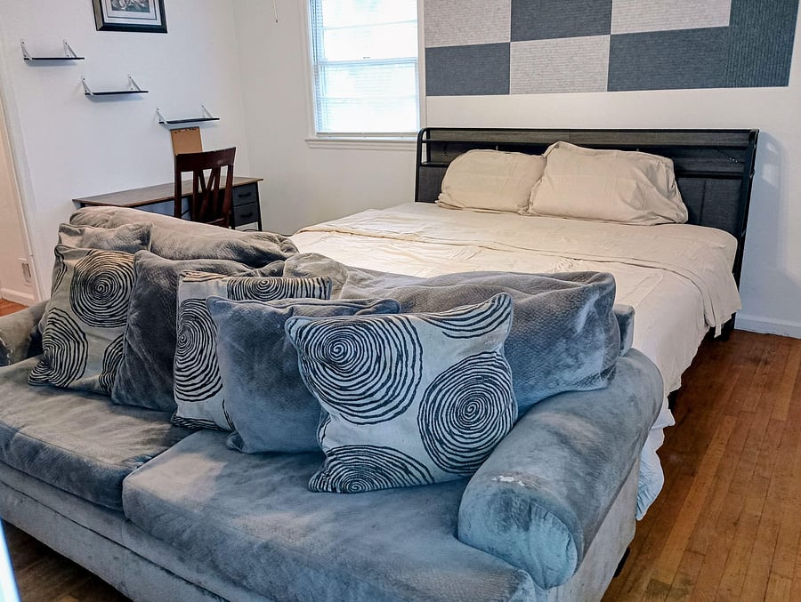 Furnished bedroom with a king bed, sofa seating, and a dedicated desk area, plus a window for natural light.