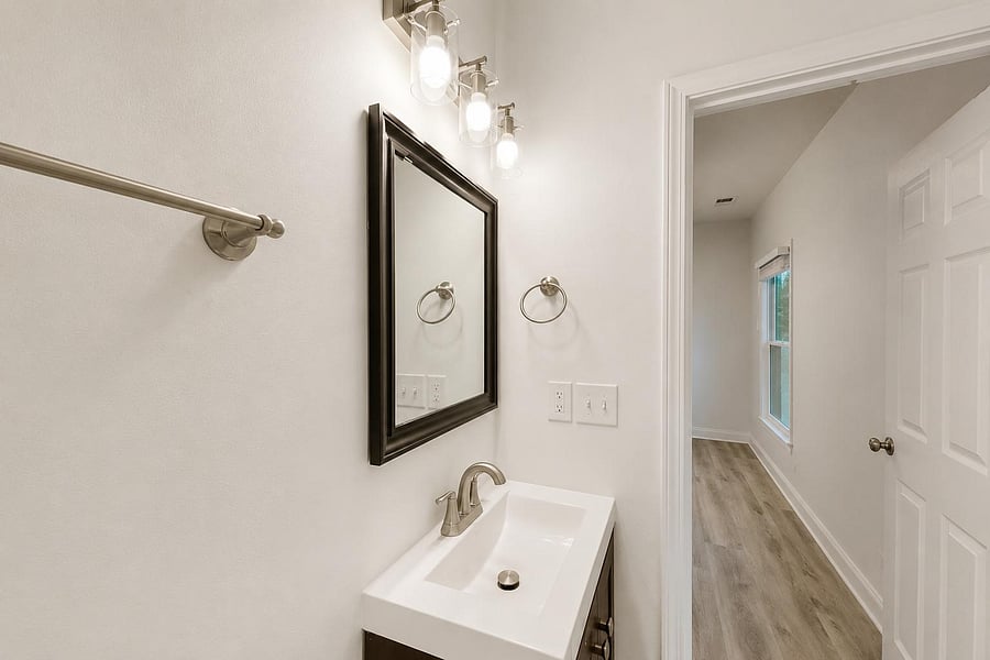 Half bath with sleek vanity, framed mirror, and updated lighting--conveniently located just off the hallway.