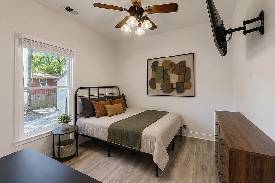 Well-sized bedroom with a large window, ceiling fan light, wall-mounted TV, and a dresser for convenient storage.