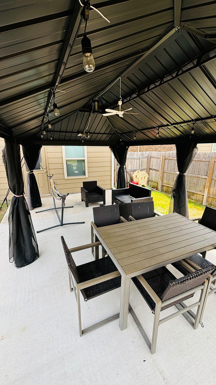 Large covered gazebo featuring closing mosquito nets, string lights, and a ceiling fan for summer days.