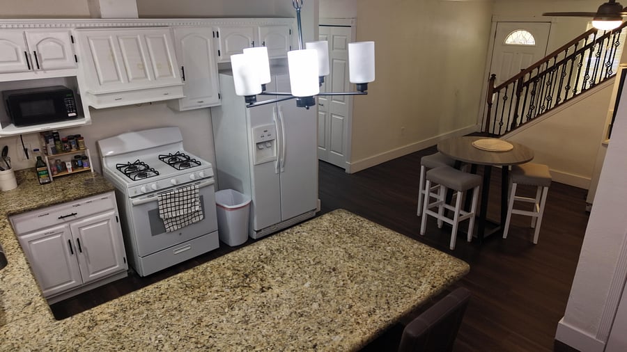 Eat-in kitchen with granite counters, ample white cabinetry, gas range, and side-by-side fridge plus a bistro table.