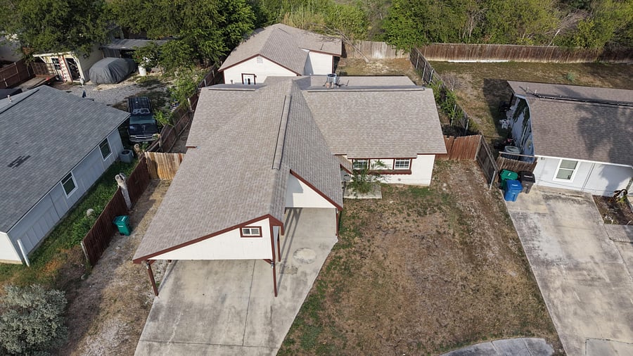 Aerial view of a fenced single-family home with driveway parking, covered entry, and a spacious backyard area.