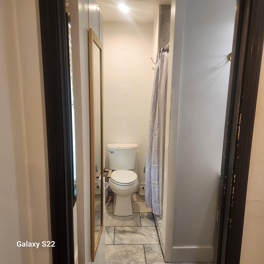 Compact bathroom with marble-look tile flooring, shower curtain, and wall-mounted hooks for everyday essentials.
