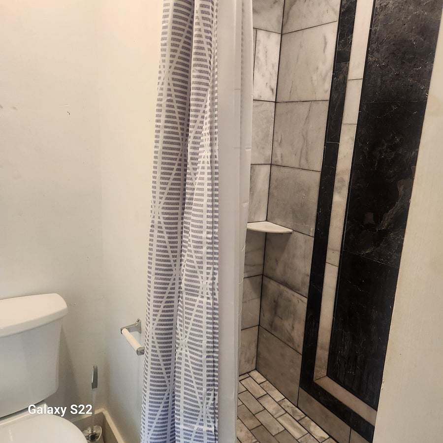Walk-in shower with tiled surround and built-in corner shelf, paired with standard toilet and neutral wall finishes.