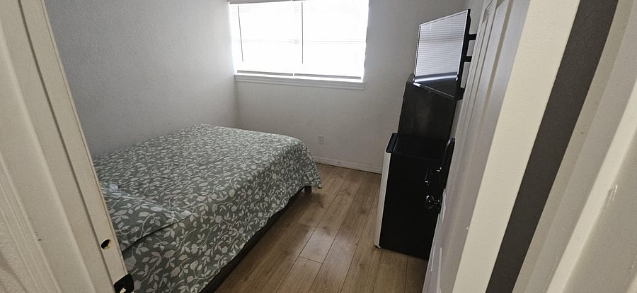 Private bedroom with a bed, wood-look flooring, and a window with blinds for natural light and privacy.