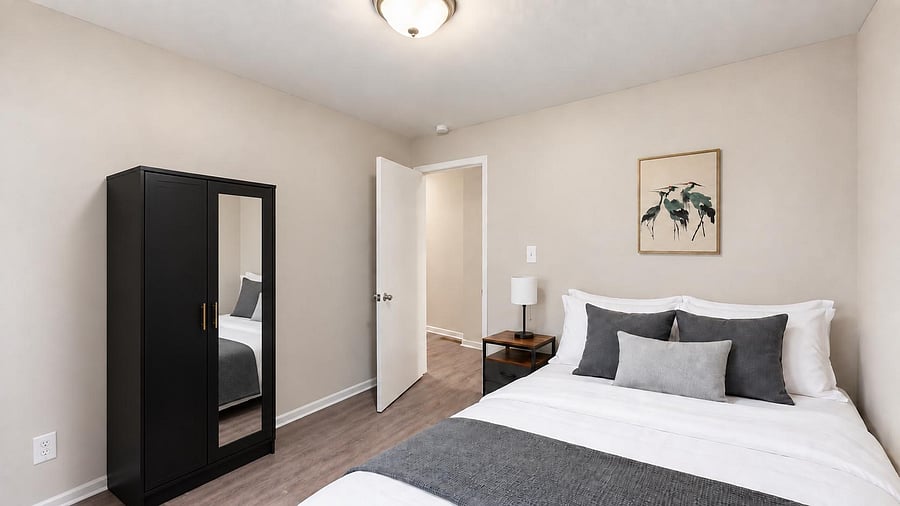 Furnished bedroom with a full bed, nightstand and lamp, plus a wardrobe with mirrored door and easy access to the hall.
