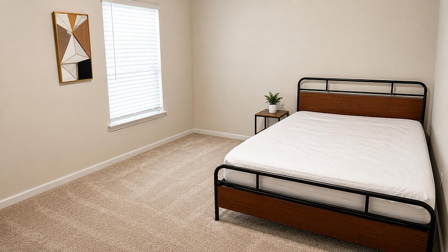 Spacious bedroom with plush carpeting, a large window with blinds, and a comfortable bed plus nightstand for easy setup.