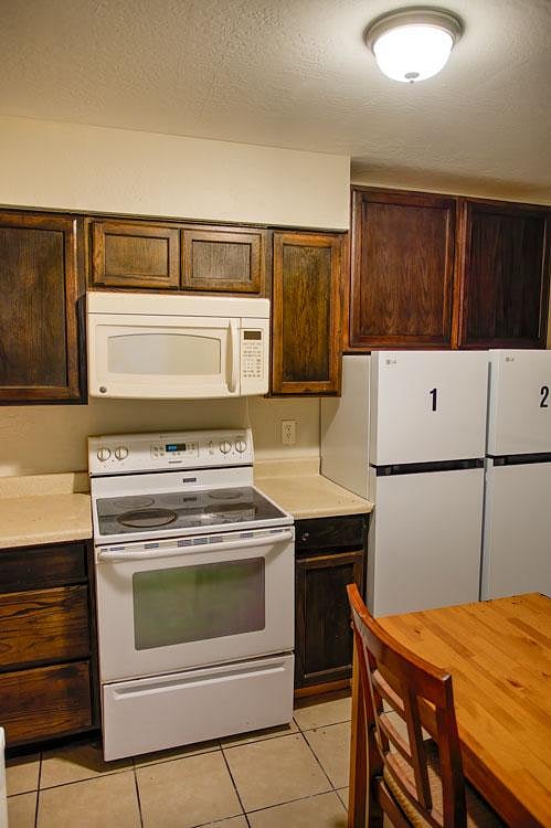 Efficient shared kitchen with ample wood cabinetry, electric range with microwave, and refrigerator access.