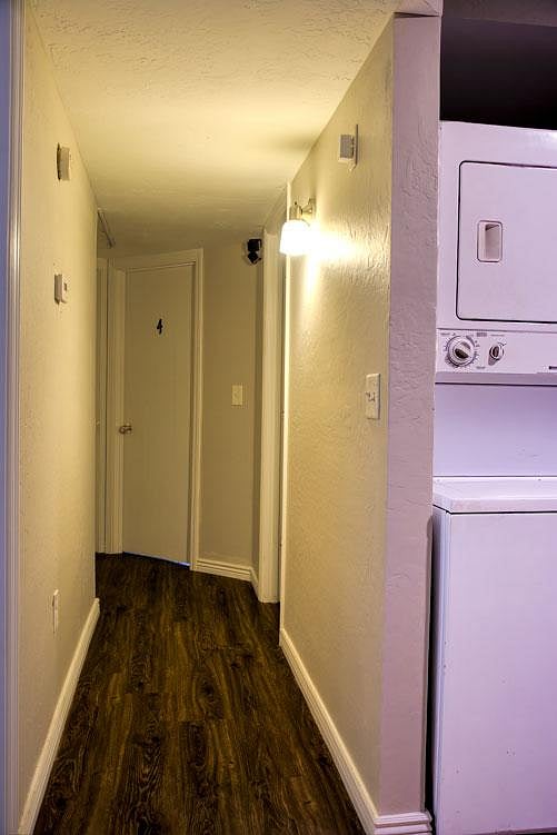 Hallway with wood-look flooring and wall lighting, plus convenient in-home stacked laundry closet near bedrooms.