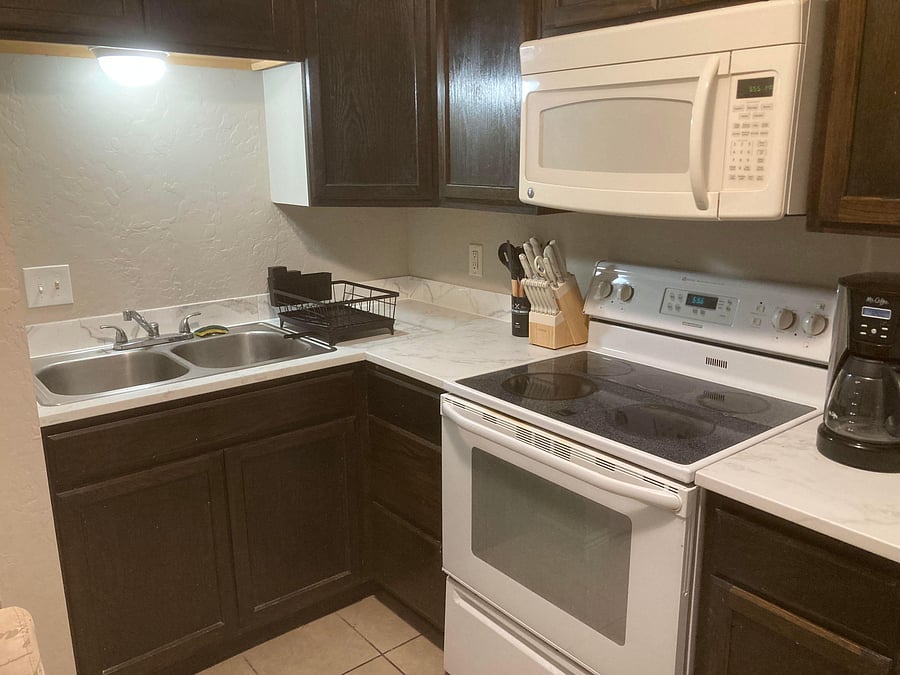 Efficient kitchen with ample cabinets, durable counters, double-basin sink, and electric range with over-the-range microwave.