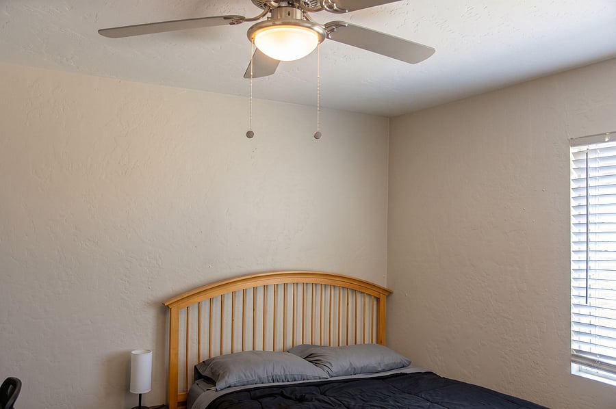 Private bedroom with a ceiling fan, window with blinds, and space for a full/queen bed and nightstand.