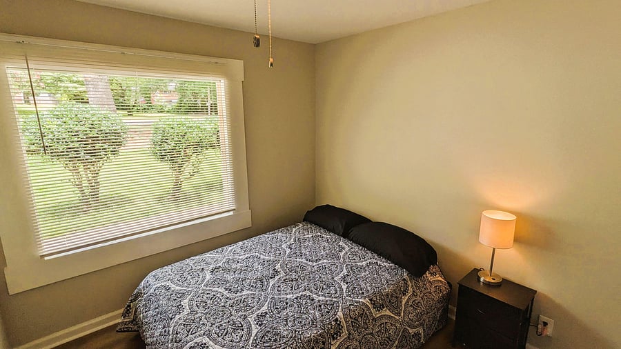 Private bedroom with a large window, blinds, and space for a full/queen bed plus a nightstand.