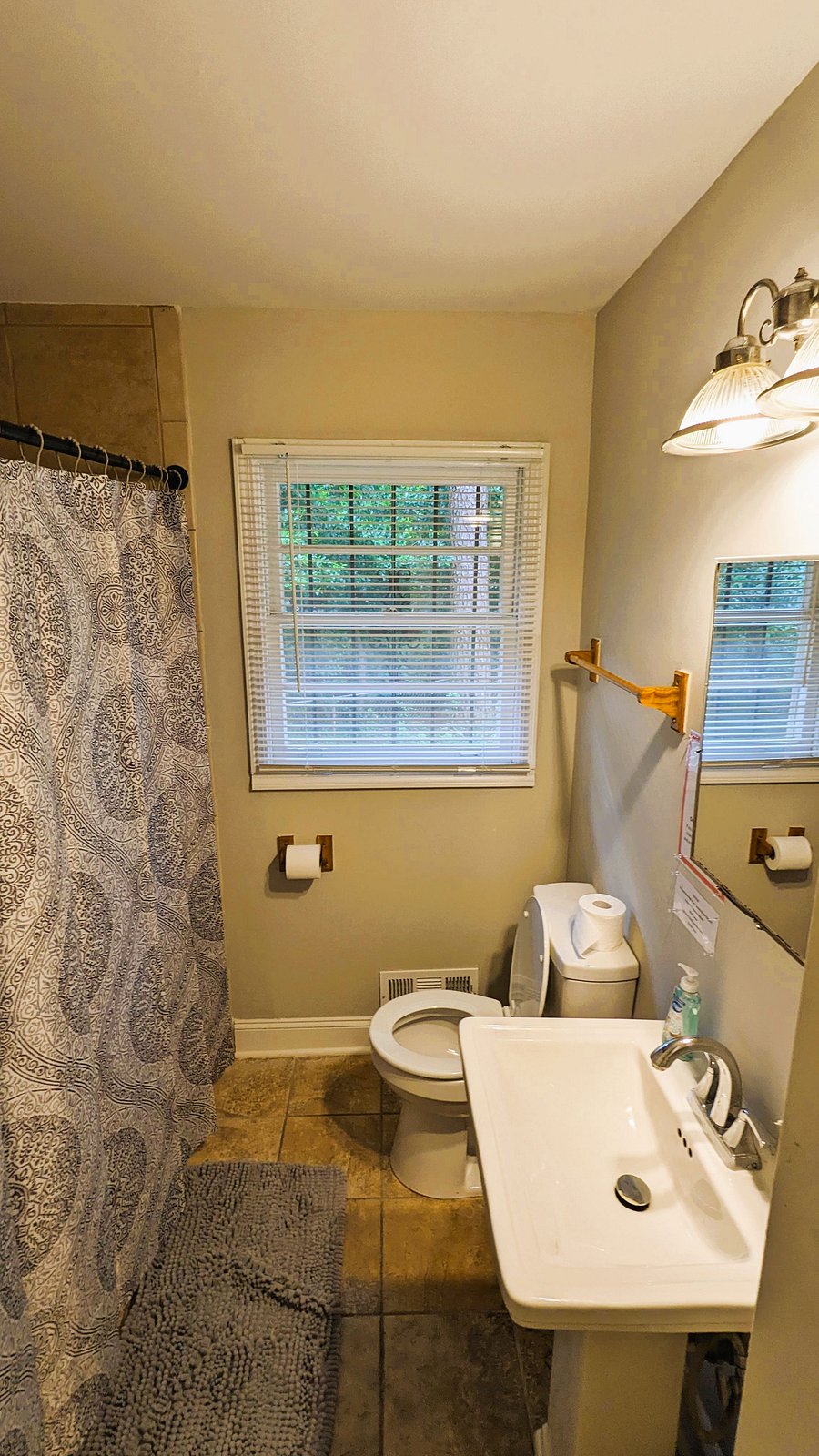 Functional full bath with tub/shower combo, tile flooring, and a vanity sink, plus a window with blinds for ventilation.