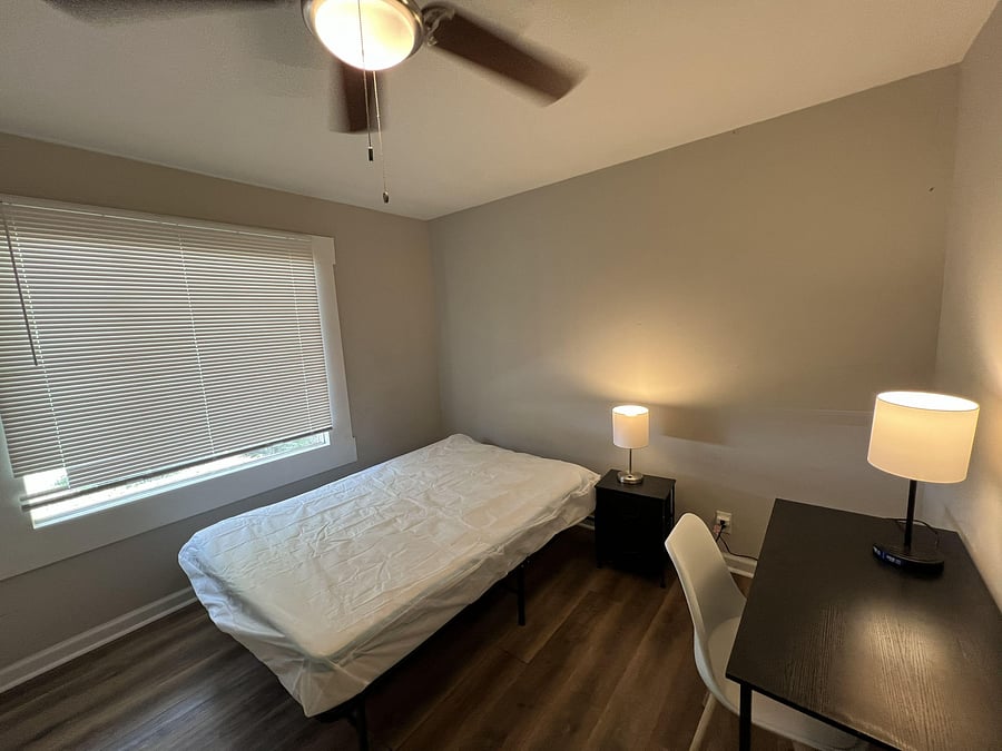 Private bedroom featuring a large window with blinds, ceiling fan, and space for a bed plus a work desk.