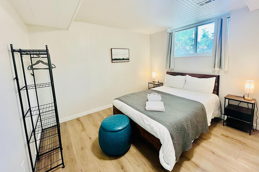 Furnished bedroom with a full bed, nightstands with lamps, and a window with curtains plus open garment storage.