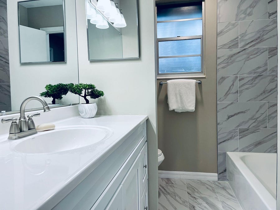 Updated bathroom with a wide vanity, mirrored medicine cabinets, and a tub/shower surround finished in marble-look tile.