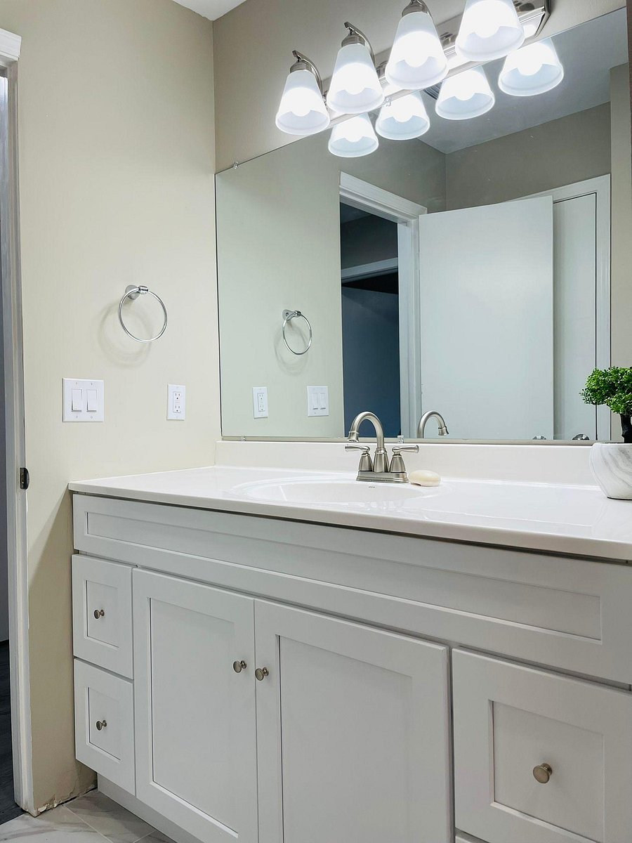Bathroom vanity features a wide mirror, ample cabinet storage, and updated lighting over a single-sink countertop.