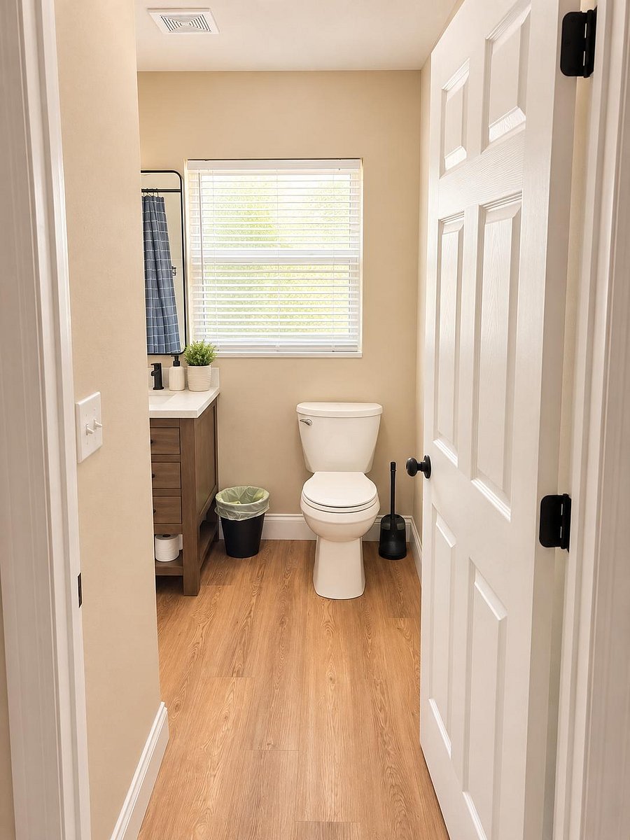 Bathroom with a double-sink vanity, wood-look flooring, and a window with blinds for ventilation and natural light.