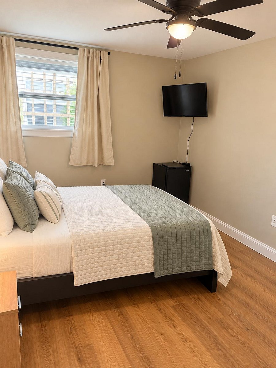Private bedroom with a full bed, window with curtains, ceiling fan, wall-mounted TV, and a mini fridge for added convenience.