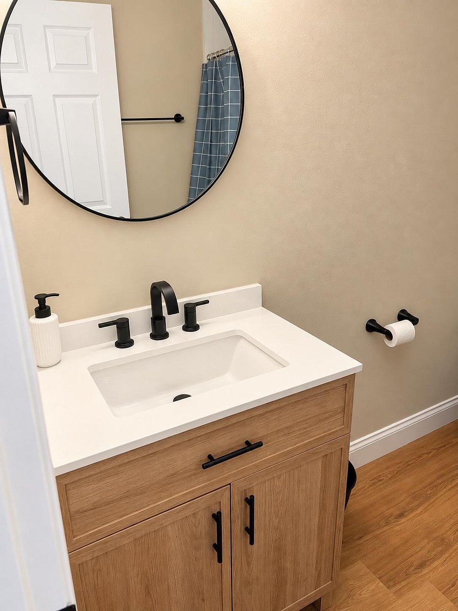 Bathroom vanity with under-sink storage, solid-surface countertop, and matte black fixtures with a round mirror.