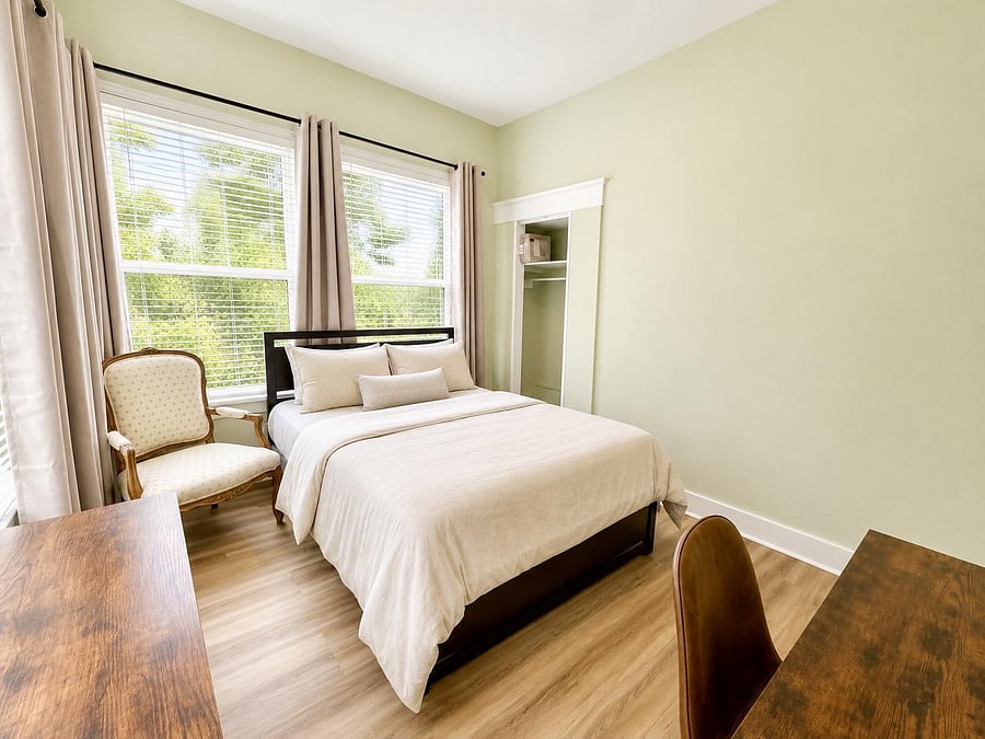 Private bedroom with large windows, a comfortable bed, desk space, and an open closet for storage.