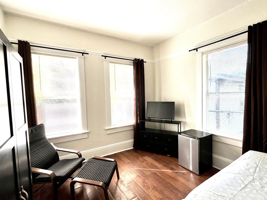 Bright sun filled room with sitting area, sleeping nook, mini fridge and comfortable chair with foot rest